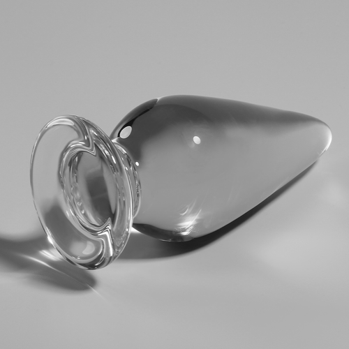 Gros plan en biais du plug anal verre borosilicate transparent forme goutte, base annelee mise en avant et corps effile brillant, surface lisse adaptable thermique.