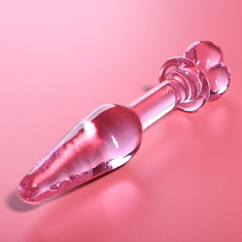 Gros plan en biais du gode anal verre borosilicate rose double embout sur fond rose, bille perlee et pointe conique brillantes, surface lisse non poreuse hygienique.