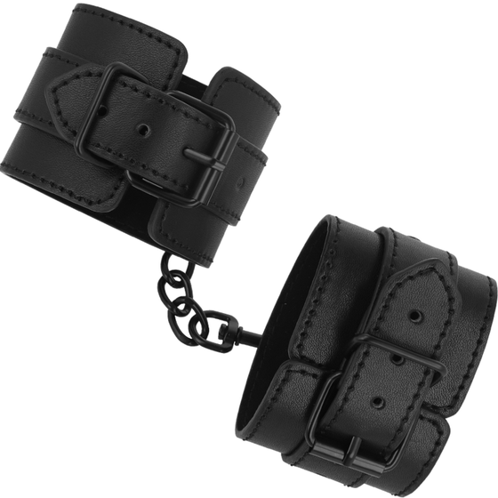 Menottes en cuir synthétique noir Intense Fetish, larges sangles à boucle reliées par une courte chaine. Restriction des poignets souple et personnalisable.