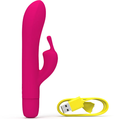 Vibromasseur rabbit fuchsia à oreilles externes et tige courbée à gauche, câble de charge jaune à droite. Double moteur en silicone pour point G et clitoris, surface lisse.