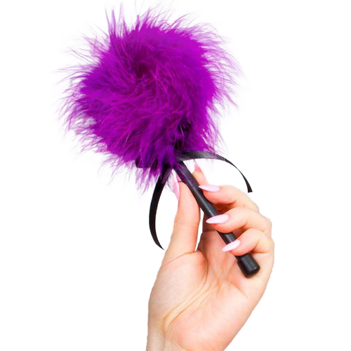 Plumeau tickler Secret Play en plumes violettes douces tenu en main par le manche noir, accessoire de caresse sensorielle pour jeux de domination douce et eveil de la peau.