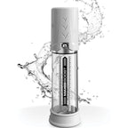Pompe a penis Max Boost avec eclaboussures d'eau soulignant l'etancheite, cylindre transparent gradue et tete blanche, dispositif piston sur fond blanc.