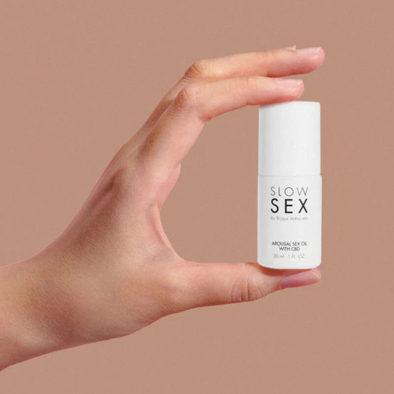 Main tenant le petit flacon Arousal Sex Oil with CBD Slow Sex Bijoux Indiscrets entre les doigts, demonstration du format compact, huile de massage intime au CBD 30 ml