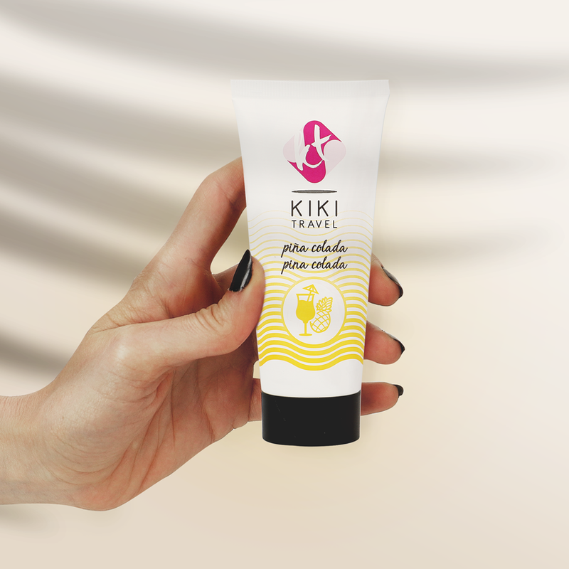 Tube de lubrifiant gourmand Pina Colada Kiki Travel tenu en main pour montrer son format compact, base eau hydratante vegan, saveur ananas coco, compatible preservatifs.