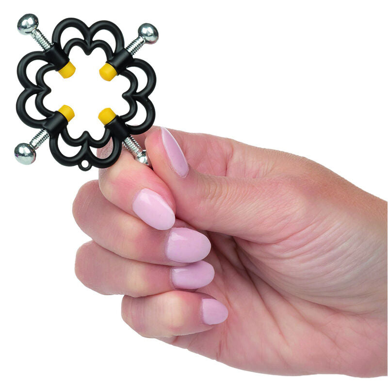 Pince à tétons Boundless florale en métal noir tenue en main, mise à l'échelle du clamp à quatre points et coussinets jaunes de cet accessoire sensoriel.