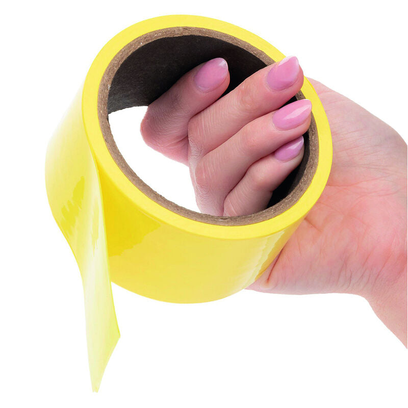 Rouleau de ruban de bondage jaune tenu en main et deroule, vinyle Boundless auto-adhesif reutilisable, montre la souplesse pour attacher en douceur.