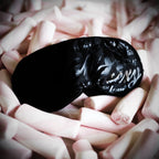 Masque sensoriel noir brillant imprimé sexy posé sur des pétales roses poudrés, bandeau textile de privation visuelle Bijoux Indiscrets pour éveiller le toucher.