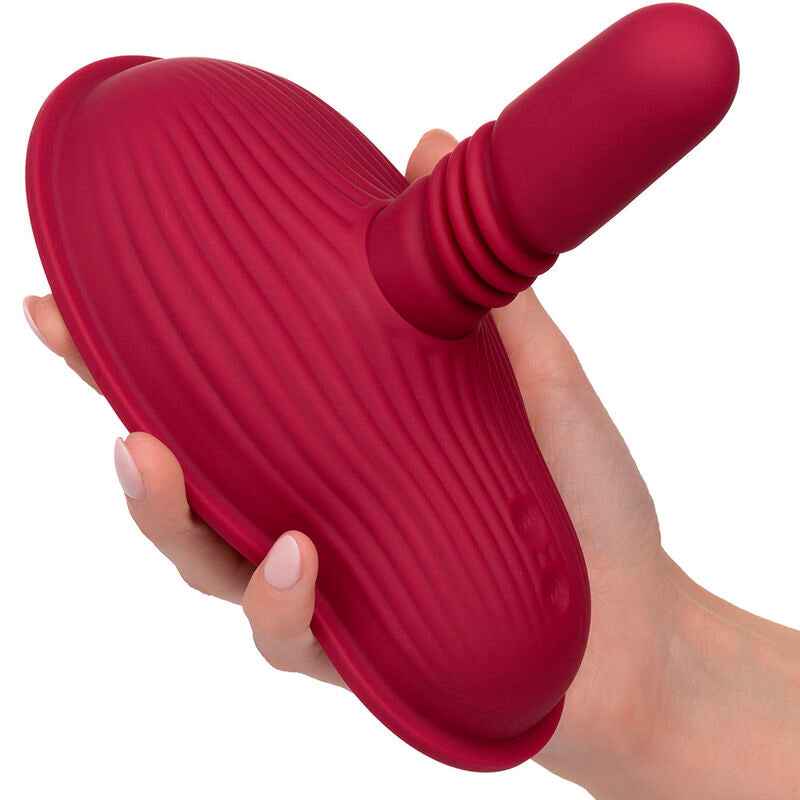 Rider Massager rouge foncé tenu en main sous un autre angle, tige centrale émergeant des doigts refermés sur la base.