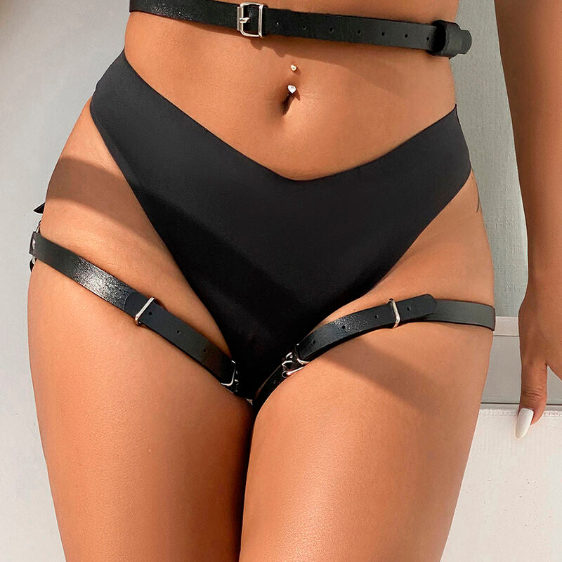 Harnais de taille et de jambes en cuir noir Subblime porte de face, ceinture a chaine sur le ventre nu et brides a noeud descendant sur la culotte noire vers les cuisses, peau visible.