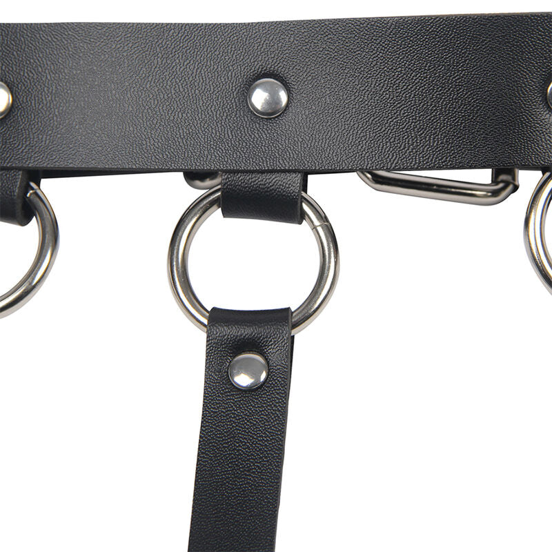 Detail de la sangle en cuir noir a anneau metal et boutons pression du harnais de poitrine Subblime, finition fetichiste soignee sur fond clair.