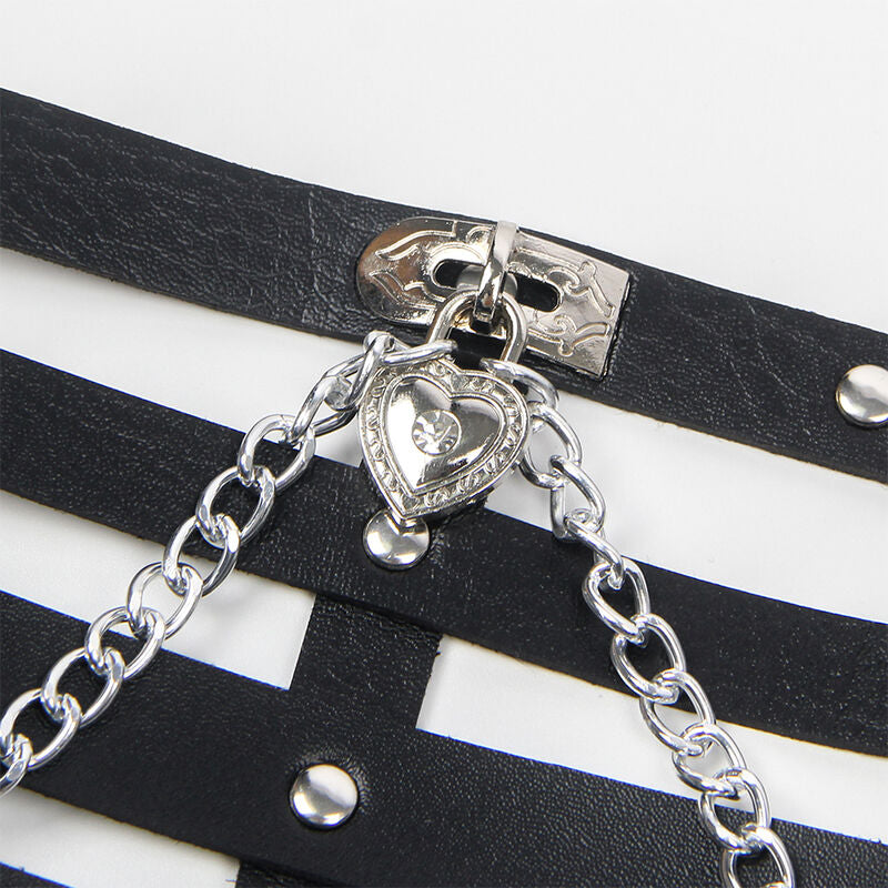 Detail du harnais corps en cuir noir Subblime avec sa chaine metal argentee et son pendentif en forme de coeur, lignes graphiques posees sur les sangles a boutons-pression.