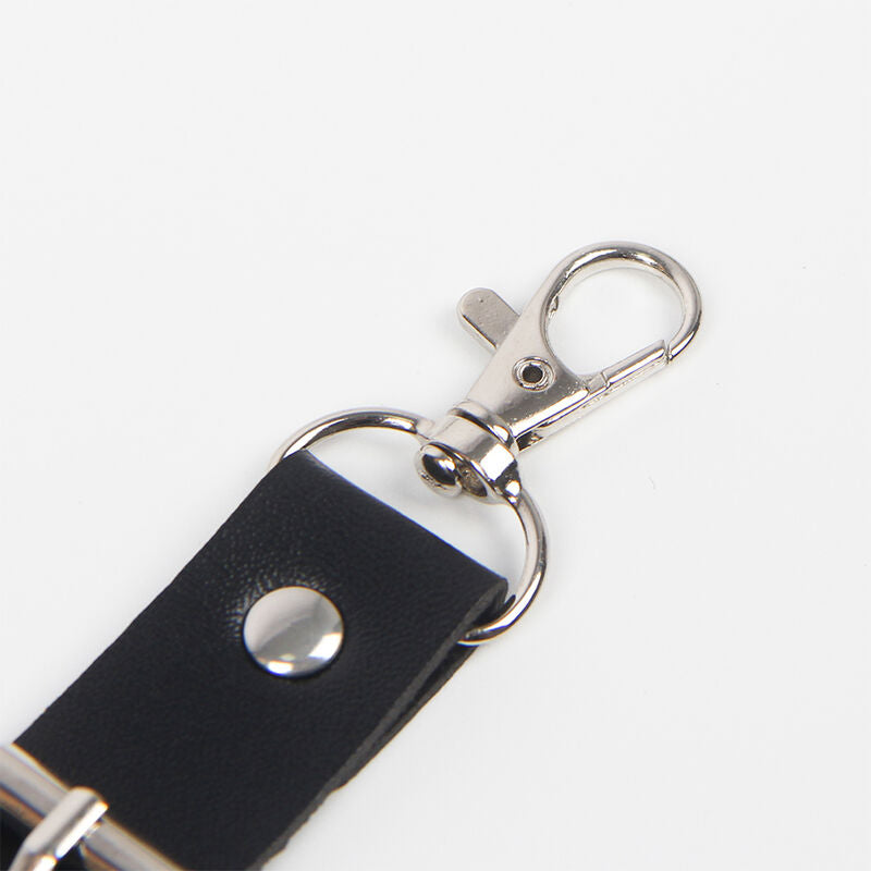 Gros plan sur le mousqueton argente et le bouton-pression du harnais en cuir noir Subblime, finition metal soignee sur sangle epaisse, accessoire fetichiste taille unique.