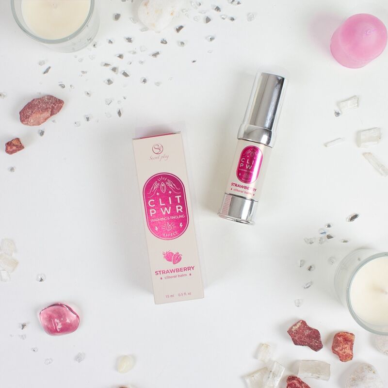 Baume clitoridien Clit Pwr fraise mis en scene avec boite et eclats decoratifs roses, flacon airless Secret Play, formule chauffante et picotante a usage externe.