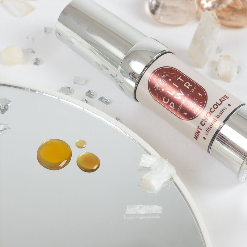 Gouttes du baume Clit Pwr menthe chocolat deposees sur un miroir pres du flacon airless. Gel stimulant clitoris a effet chauffant et picotant, absorption rapide, usage externe.