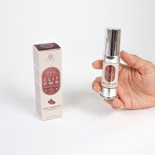 Flacon airless du baume clitoris Clit Pwr menthe chocolat tenu en main pres de sa boite cuivre. Soin stimulant externe a sensation de chaleur, sans effet collant, saveur gourmande.