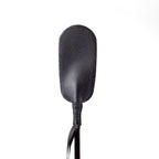Cravache ovale en cuir synthetique noir, embout plat en forme de palette et tige fine. Accessoire BDSM leger pour des sensations du frolement a la claque, presente de face.