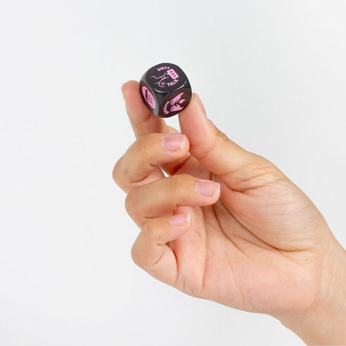 De preliminaire en silicone noir et rose tenu entre deux doigts, face illustree visible. Jeu de des de 20 mm proposant six options coquines, discret et nomade pour le couple.