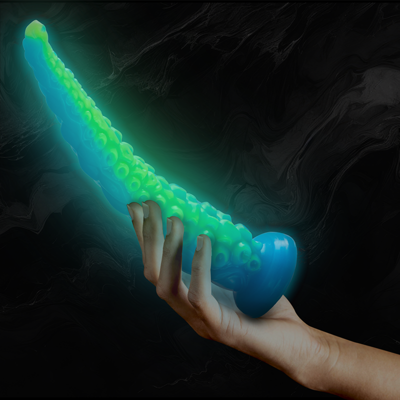 Gode tentacule fin fluorescent bleu et vert tenu en main sur fond noir, mettant en valeur sa longueur souple et sa lueur phosphorescente qui brille dans l'obscurite