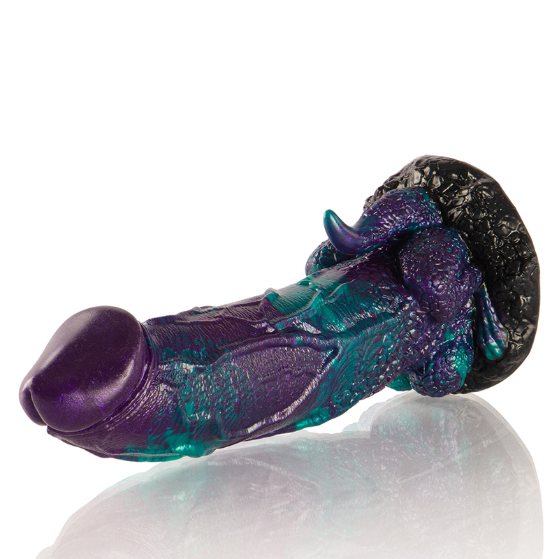 Gode fantasy en silicone violet et turquoise couche de profil, relief sculpte et base granuleuse. Finition patinee aux reflets brillants, matiere souple inspiree d'un mythe.