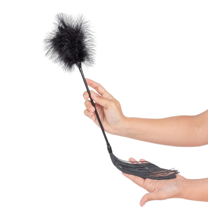 Duster plumes et fouet noir tenu en main montrant le cote lanieres, plumeau visible au bout. Accessoire BDSM double usage pour explorer la sensorialite a deux.