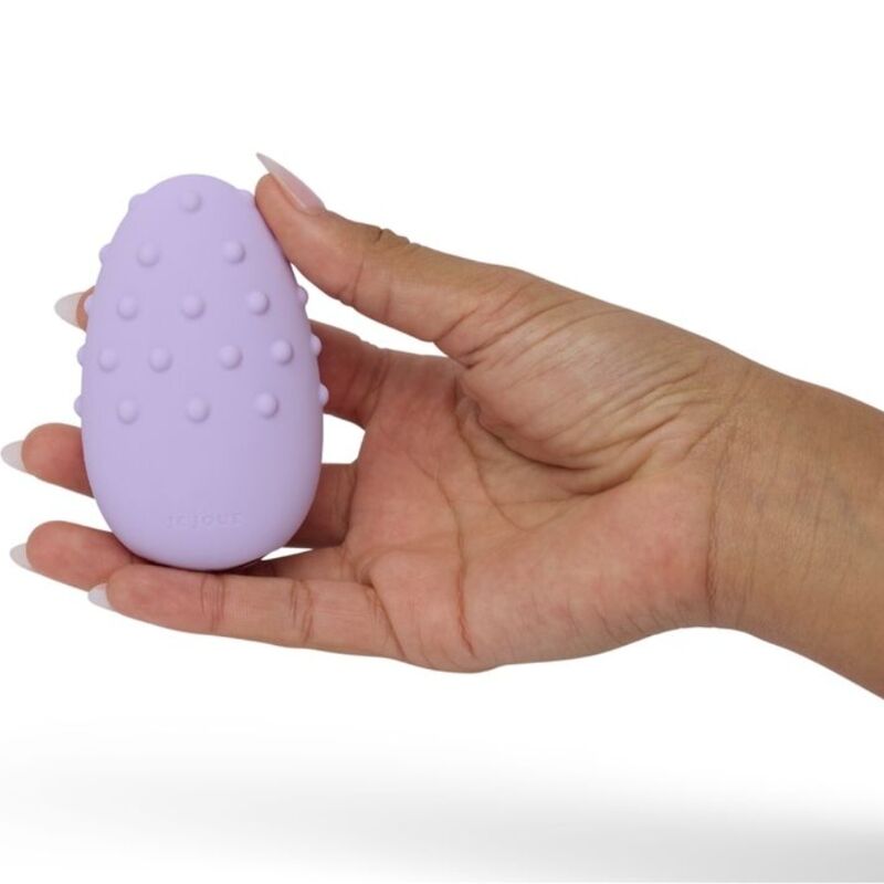 Mimi Deux lilas posé à plat sur une main ouverte, surface crêtée de reliefs bien visible, plan illustrant la taille compacte du galet vibrant en silicone sur fond blanc parfaitement épuré.