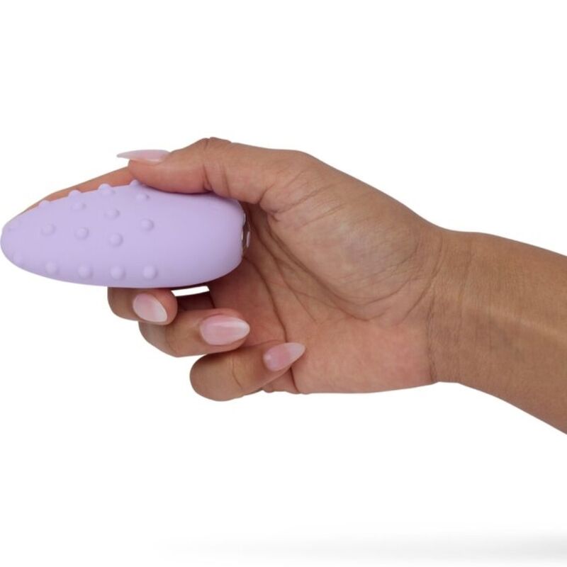 Masseur Mimi Deux lilas saisi à pleine main, galet texturé de picots enveloppé par les doigts repliés, vue rapprochée montrant la prise et la taille du produit sur fond blanc épuré.