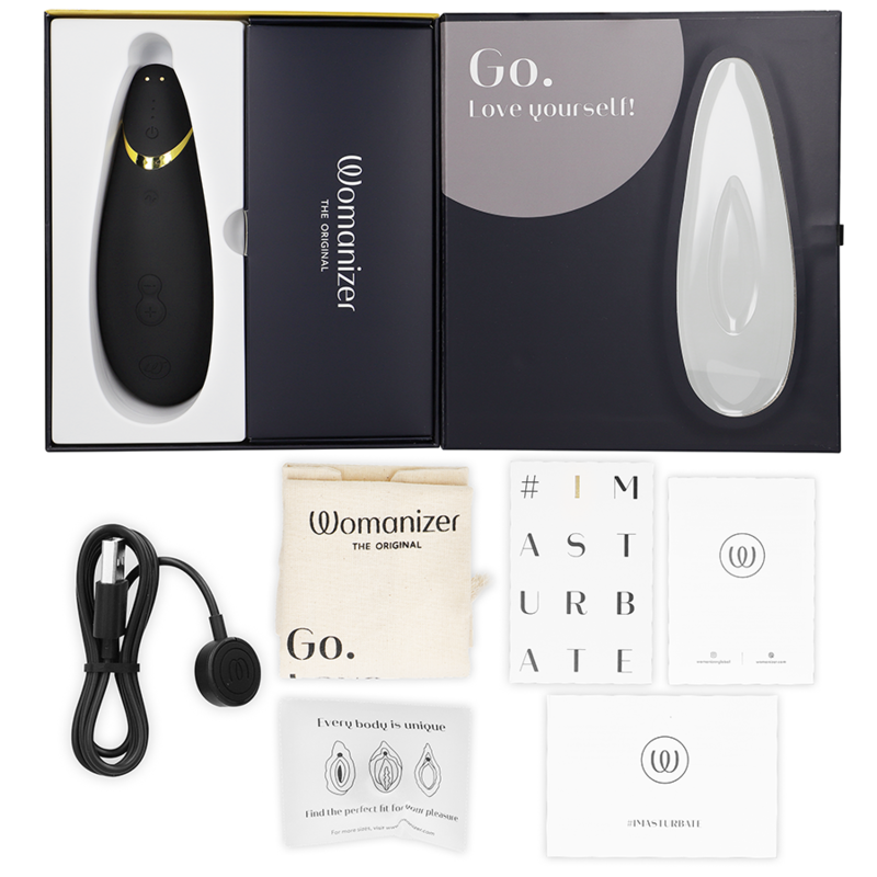 Coffret noir ouvert du Womanizer Premium 2, câble de charge, sachet et cartes de notice à plat, stimulateur clitoridien noir rechargeable par ondes d'air.