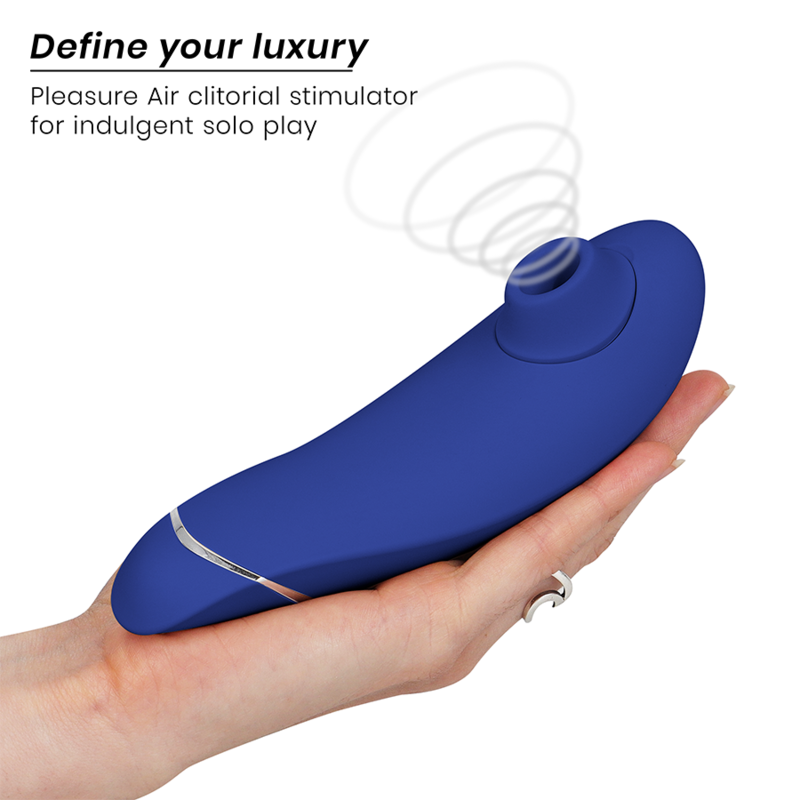 Main ouverte présentant le Womanizer Premium 2 bleu au liseré argenté posé à plat, embout d'air pulsé vers la gauche, schéma d'ondes d'air clitoridien.
