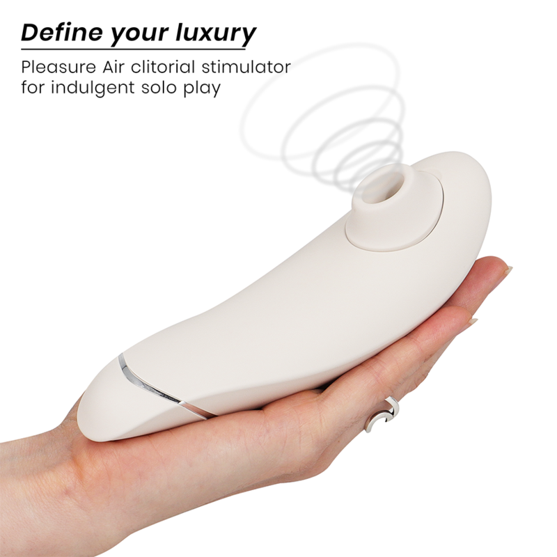 Main ouverte présentant le Womanizer Premium 2 blanc au liseré argenté posé à plat, embout d'air pulsé vers la gauche, schéma d'ondes d'air clitoridien.