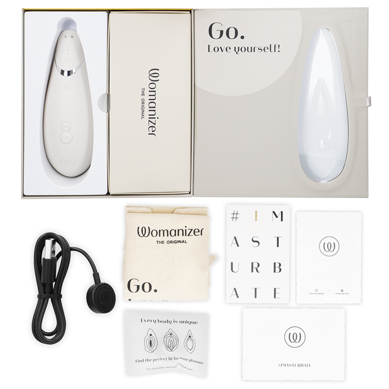 Coffret beige ouvert du Womanizer Premium 2, câble de charge, sachet et cartes de notice à plat, stimulateur clitoridien blanc rechargeable par ondes d'air.