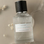 Gros plan du flacon de parfum aux phéromones Unscented Eye Of Love, verre strie au bouchon bois fonce, eau de parfum inodore 50 ml posee sur fond beige fleuri.