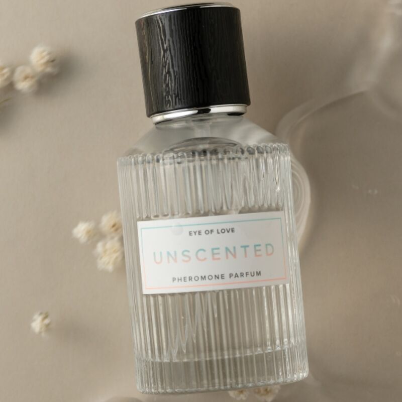 Gros plan du flacon de parfum aux phéromones Unscented Eye Of Love, verre strie au bouchon bois fonce, eau de parfum inodore 50 ml posee sur fond beige fleuri.
