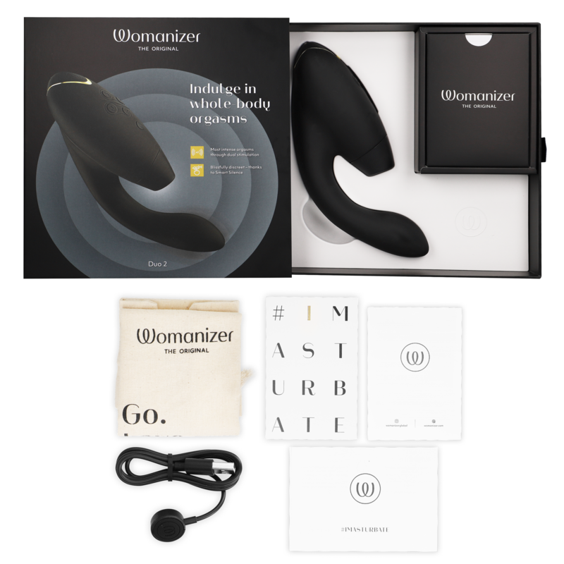 Coffret noir ouvert du Womanizer Duo 2, câble de charge, sachet et cartes de notice à plat, double stimulateur clitoris et point G rechargeable. Présentation complète du coffret cadeau.