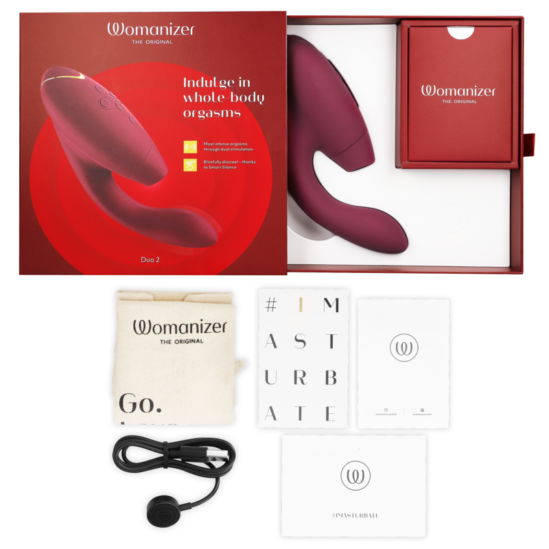 Coffret rouge ouvert du Womanizer Duo 2, câble de charge, sachet et cartes de notice à plat, double stimulateur bordeaux clitoris et point G rechargeable.