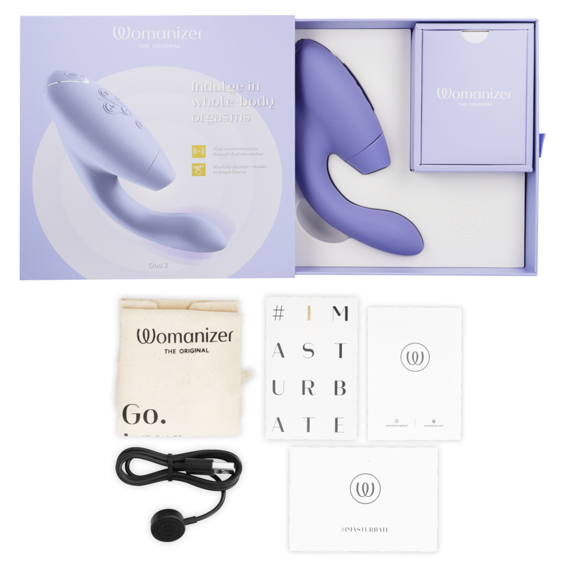 Coffret violet du Womanizer Duo 2 ouvert avec le stimulateur dans son écrin, accompagné du câble USB, de la pochette et des cartes d'accessoires sur fond clair.