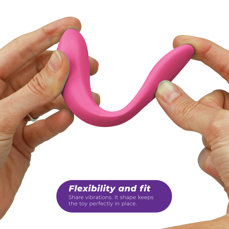 Vibromasseur couple We-Vibe en silicone rose framboise étiré entre les deux mains pour démontrer sa souplesse, sa forme en U et son maintien parfait pendant les rapports.