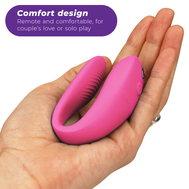 Vibromasseur couple We-Vibe en silicone rose framboise posé au creux d'une main, vue trois-quarts soulignant sa forme en U compacte conçue pour être portée pendant l'amour.
