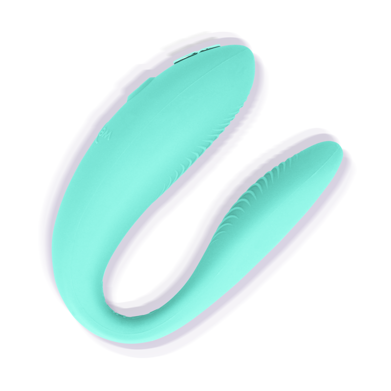 Vibromasseur couple We-Vibe en silicone vert turquoise en forme de U, vue trois-quarts isolée sur fond blanc, dévoilant les deux branches souples à porter pendant les rapports.