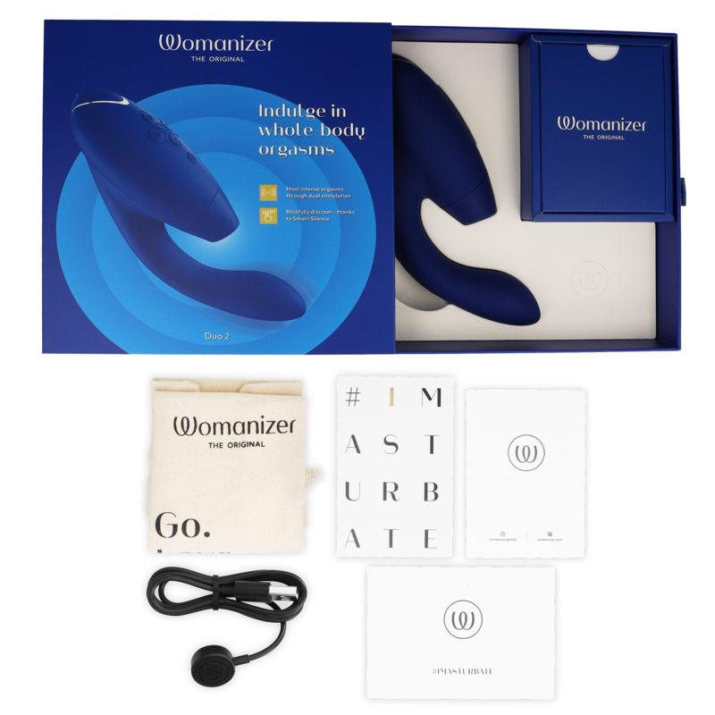 Coffret bleu ouvert du Womanizer Duo 2 avec stimulateur clitoridien et vaginal logé dans son écrin, à côté du câble USB, de la pochette et des cartes d'accessoires.