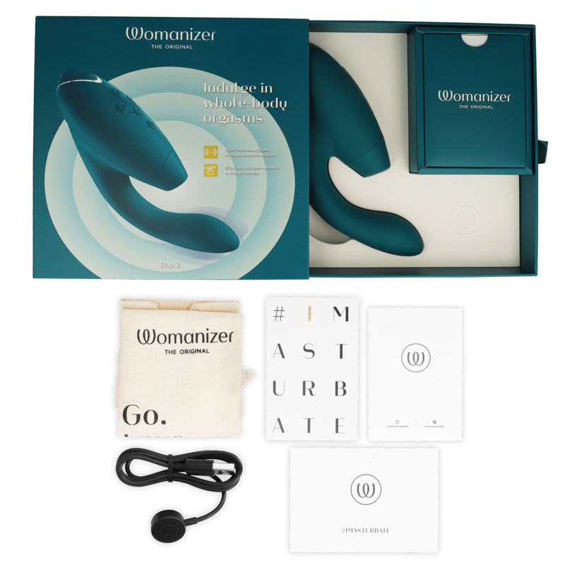 Coffret clair du Womanizer Duo 2 ouvert sur fond beige avec stimulateur, câble de charge USB, pochette de rangement et cartes d'accessoires disposés autour.