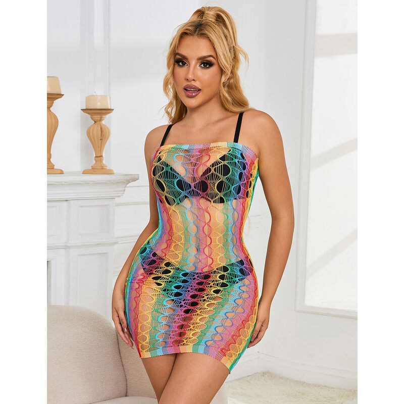 Mini-robe resille arc-en-ciel Subblime a bretelles devant une cheminee claire, maille multicolore transparente revelant la peau du buste.
