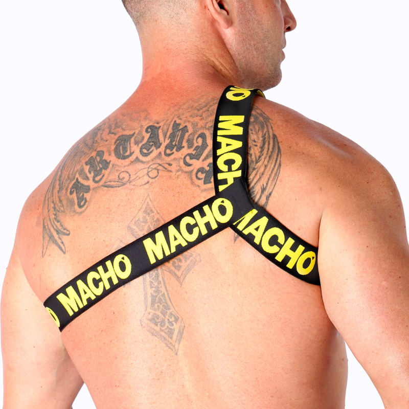Harnais homme Macho à sangles rouges vu de profil sur torse nu musclé tatoué, bande logo sur l'épaule, illustrant un style fétichiste coloré et la coupe ajustée près du corps.
