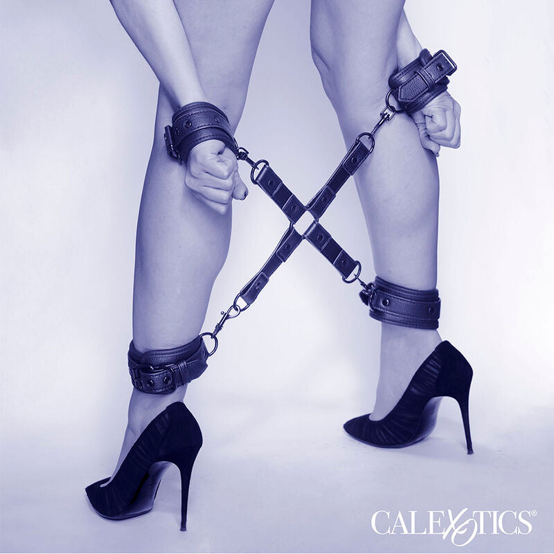 Plan de jambes nues en escarpins et poignets entraves par le kit hog tie Nocturnal en croix, visuel d'ambiance CalExotics du systeme de contrainte.