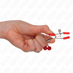 Pince a tetons rouge a grelots tenue en main sous un angle rapproche, mise en valeur du serrage progressif et de la touche coloree, accessoire Kink.