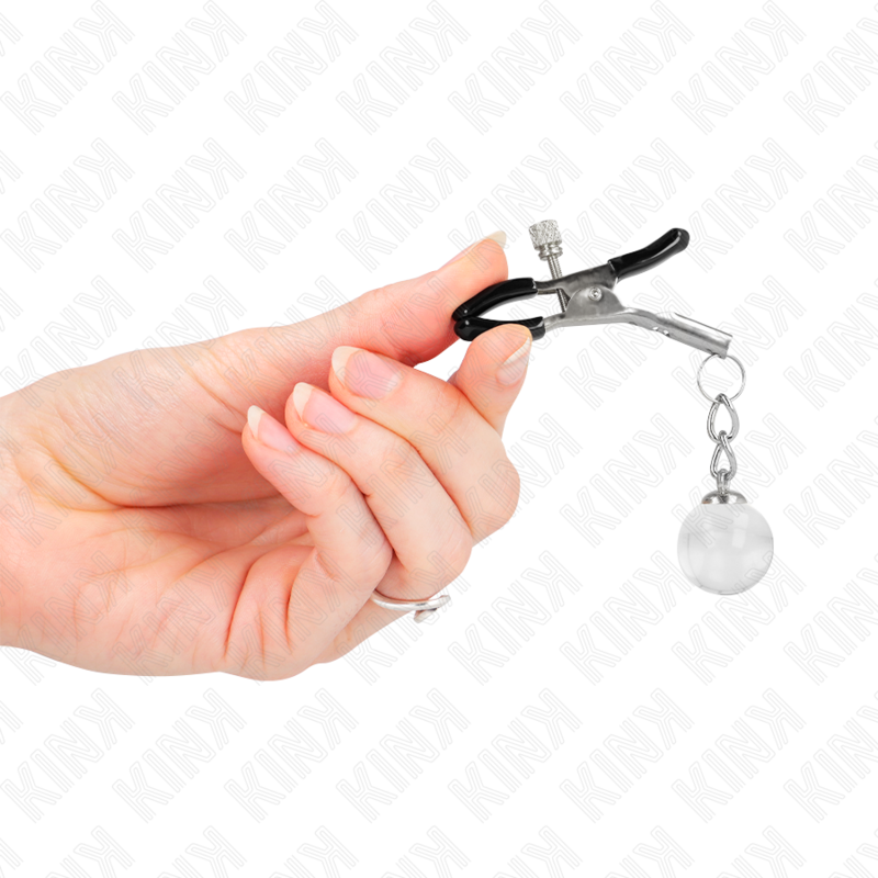 Pince a tetons a embout noir et bille de verre transparente tenue entre les doigts, mise en valeur de la traction par le lest, accessoire Kink.