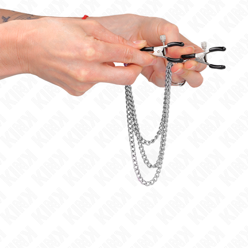 Pinces a tetons en metal reliees par une chaine argentee a triple rang tenues en main, poids et tension au mouvement, accessoire BDSM Kink.