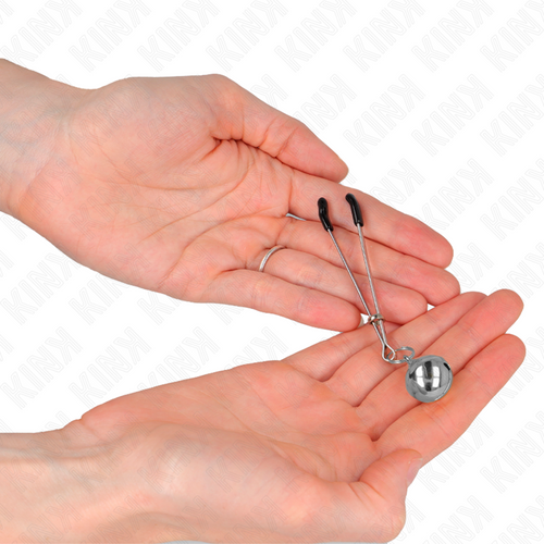 Pince a tetons argentee a grelot tenue dans une main ouverte, gros plan. Accessoire de stimulation par pincement aux embouts proteges pour les jeux a deux.