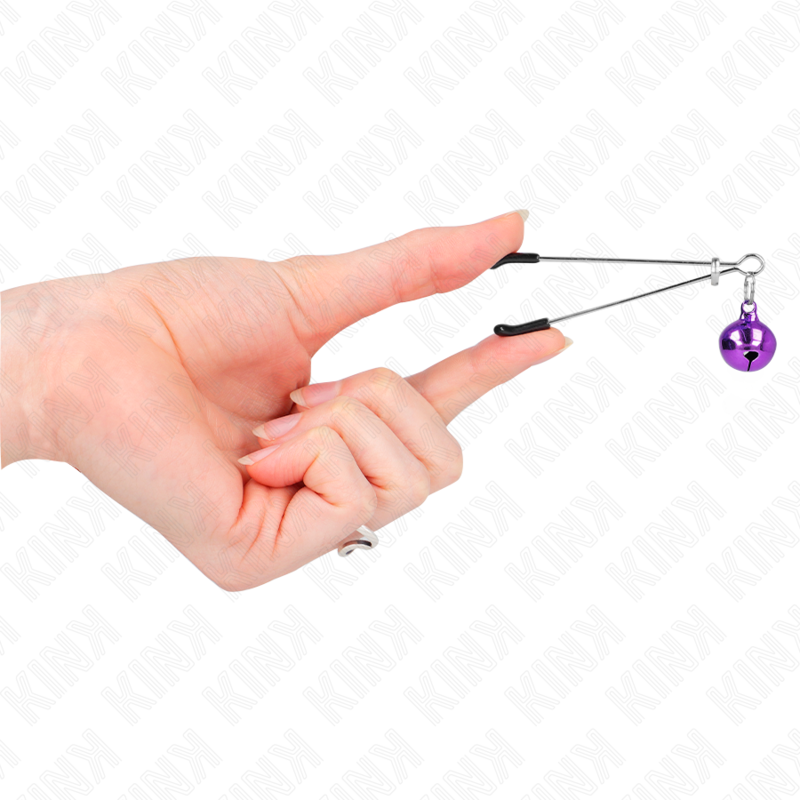 Pince a tetons fine a grelot violet tenue entre les doigts, mise en valeur du serrage delicat et du pendentif sonore, accessoire BDSM Kink.