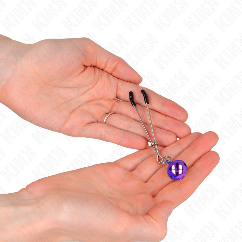 Pince a tetons en metal a grelot violet tenue au creux des mains, gros plan sur la finesse du profil pour une stimulation ciblee, gamme Kink.