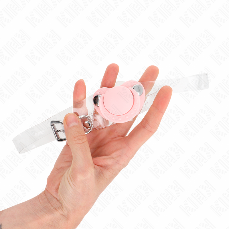 Bâillon sucette rose en silicone tenu au creux de la main, échelle visible, avec sa sangle limpide et sa boucle réglable, accessoire de soumission compact et léger.